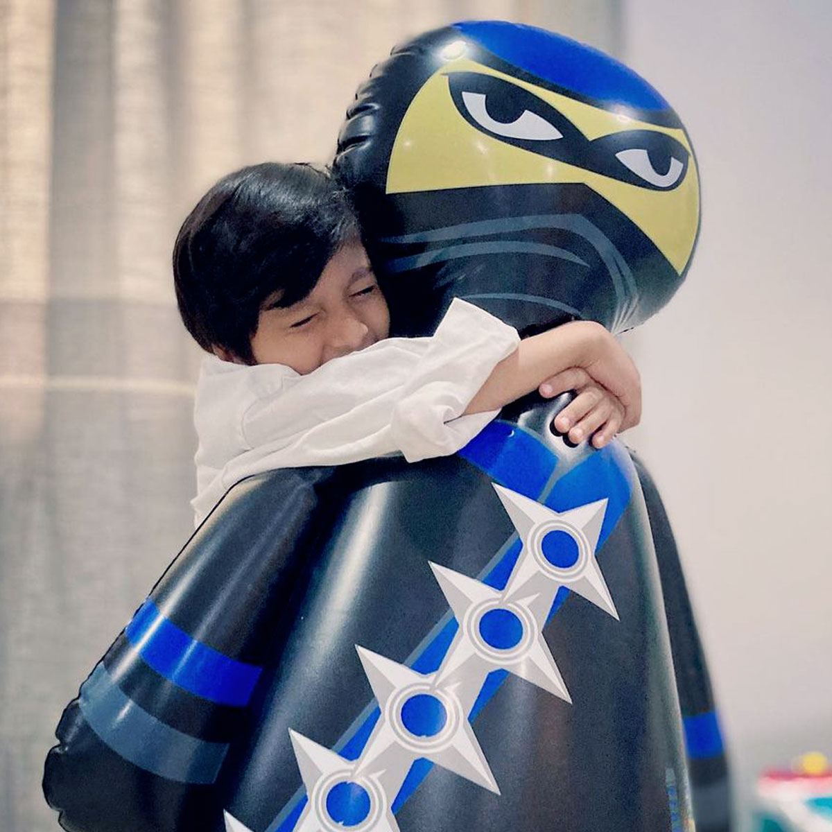 Nobi the Ninja the inflatable punching bag gets a hug from a kid in a karate uniform.
