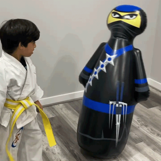 Boy in karate uniform punching the Inflatable Dudes® NOBI kids punching bag.